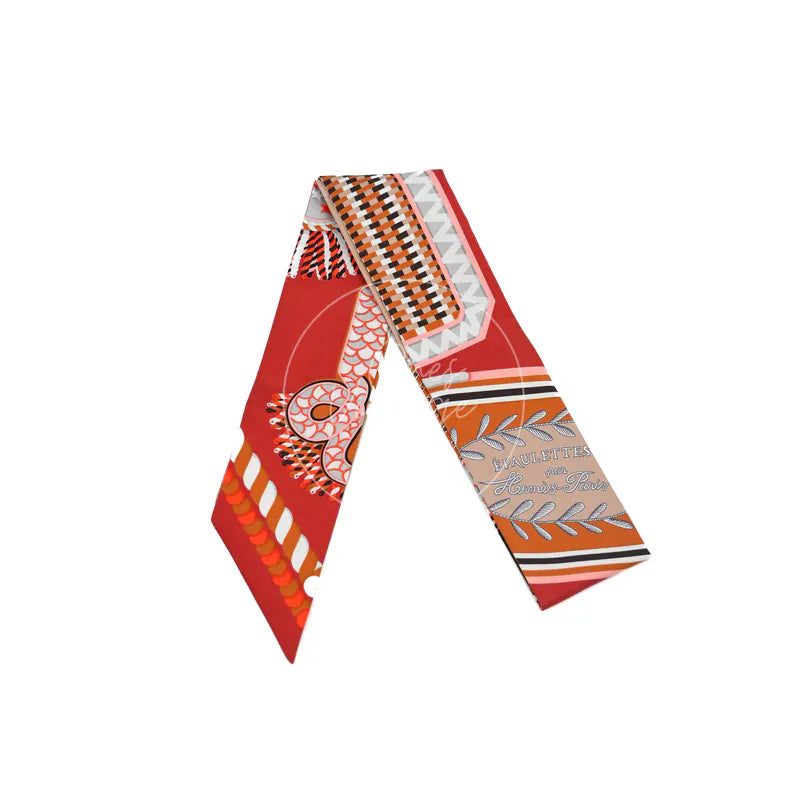 Hermès Epaulettes de Gala Twilly in orange silk 100%, featuring red and orange color-blocked print and patterned silk twilly scarf, front view