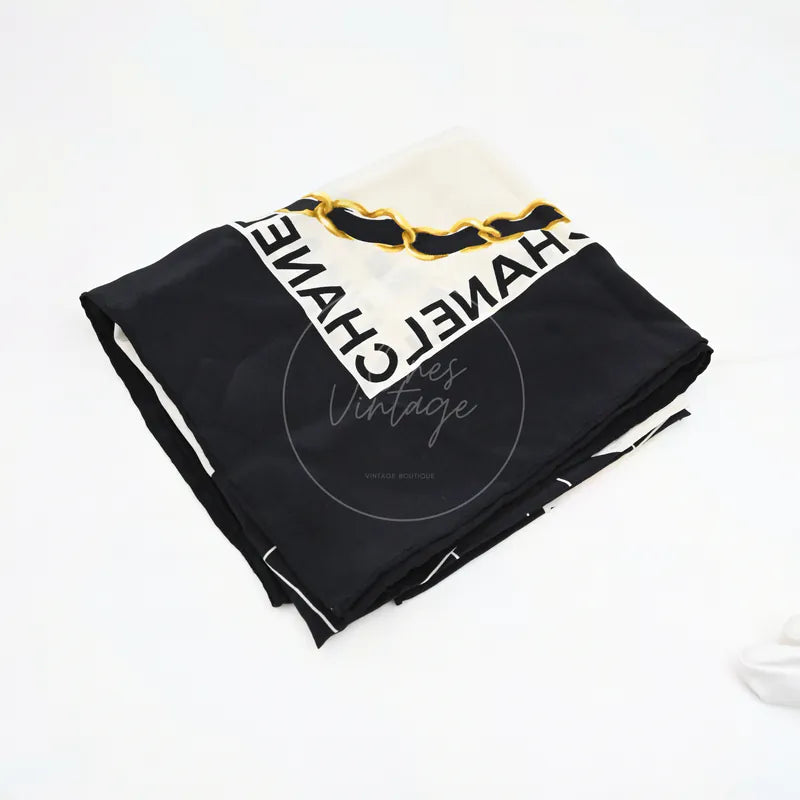 Chanel and Scarf in black and white silk, featuring folded black-and-white scarf and bold Chanel lettering border, front three-quarter view