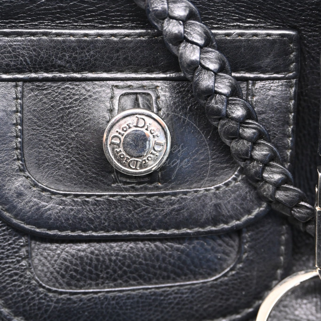 Close-up of engraved Dior logo button on front pocket and braided leather strap