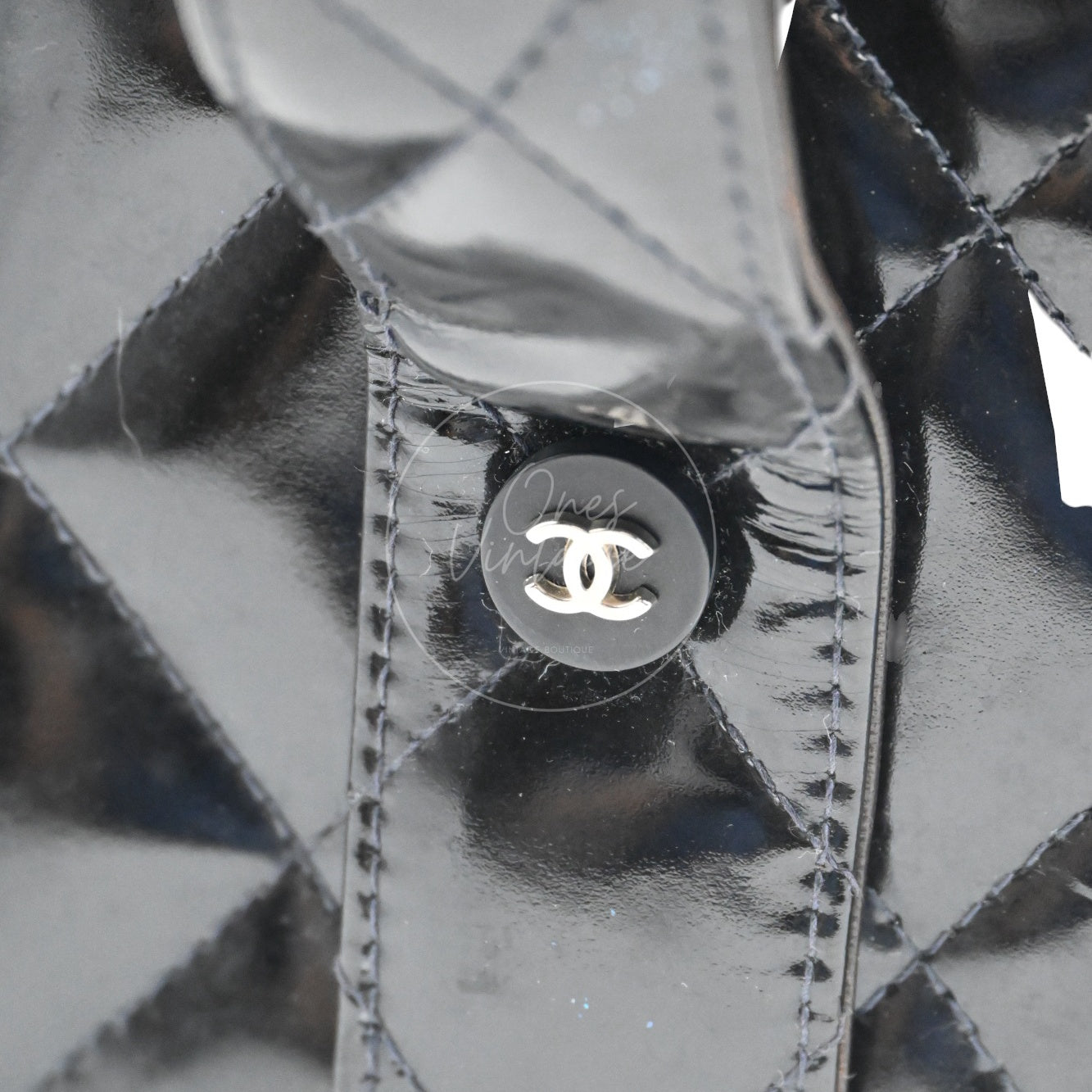 Close-up of small black button with silver-tone metal CC logo on the leather strap side