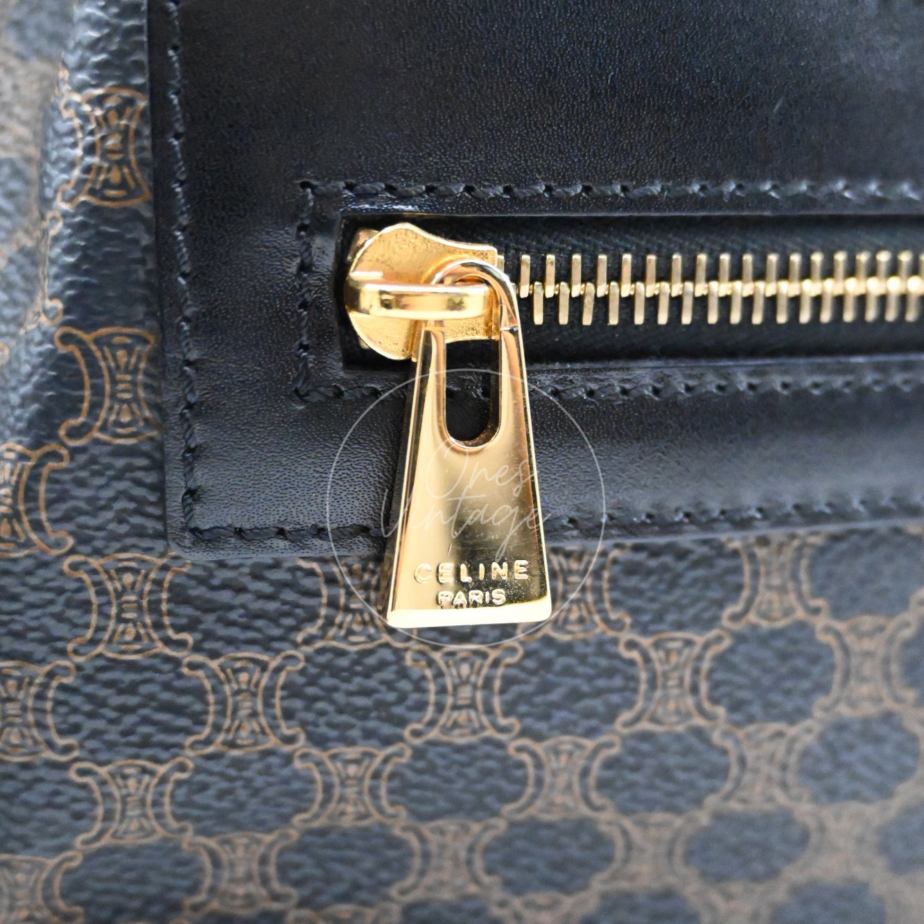 Close-up of vintage gold-tone zipper pull engraved with CELINE PARIS logo on black macadam canvas