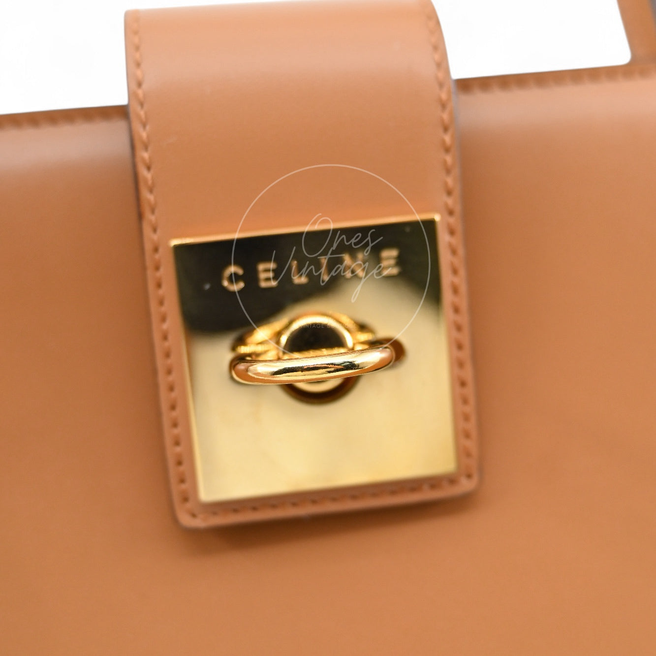Close-up of Céline vintage engraved gold hardware door-knocker lock on tan leather