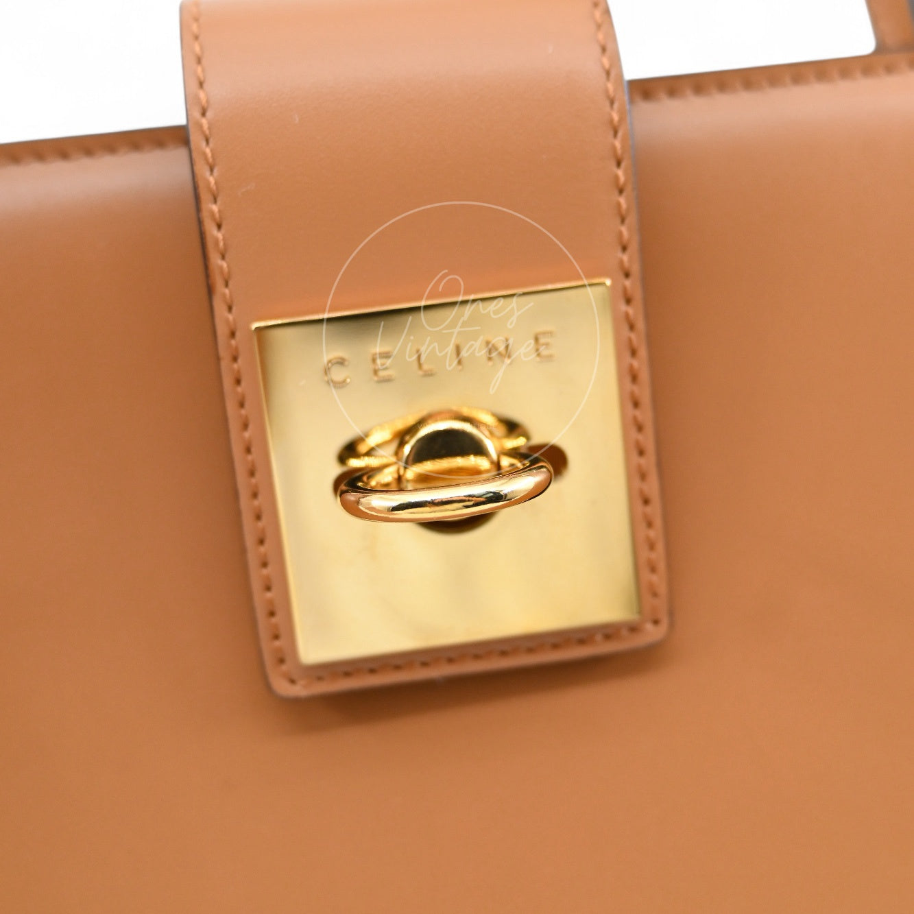 Close-up of Céline vintage engraved gold hardware door-knocker lock on tan leather