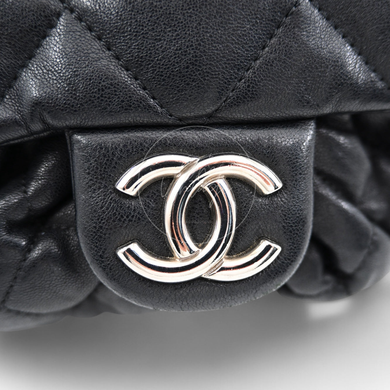Close-up of shiny silver-tone interlocking CC turn-lock hardware on black leather flap