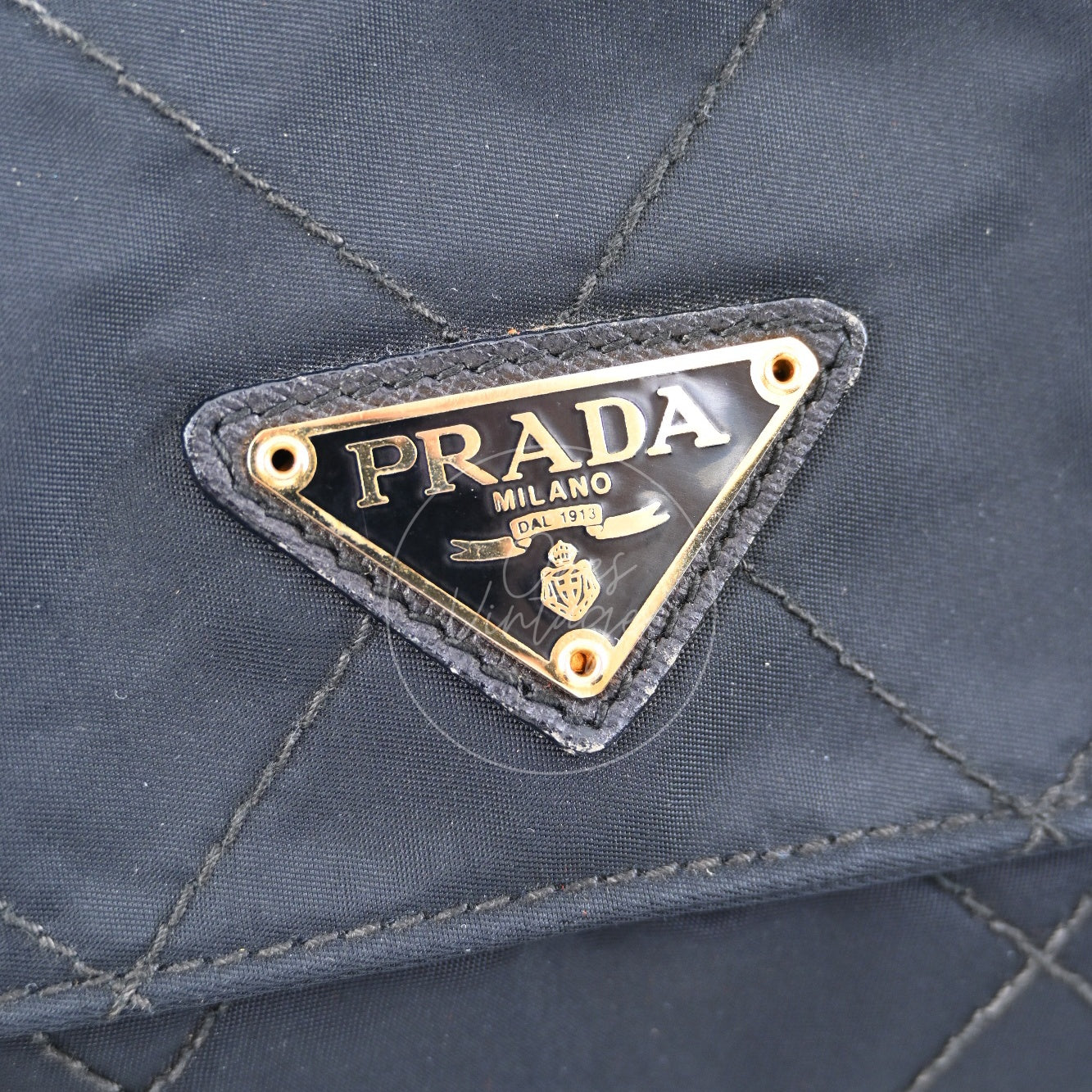 Close-up of Prada signature black enamel triangle metal logo badge on quilted nylon