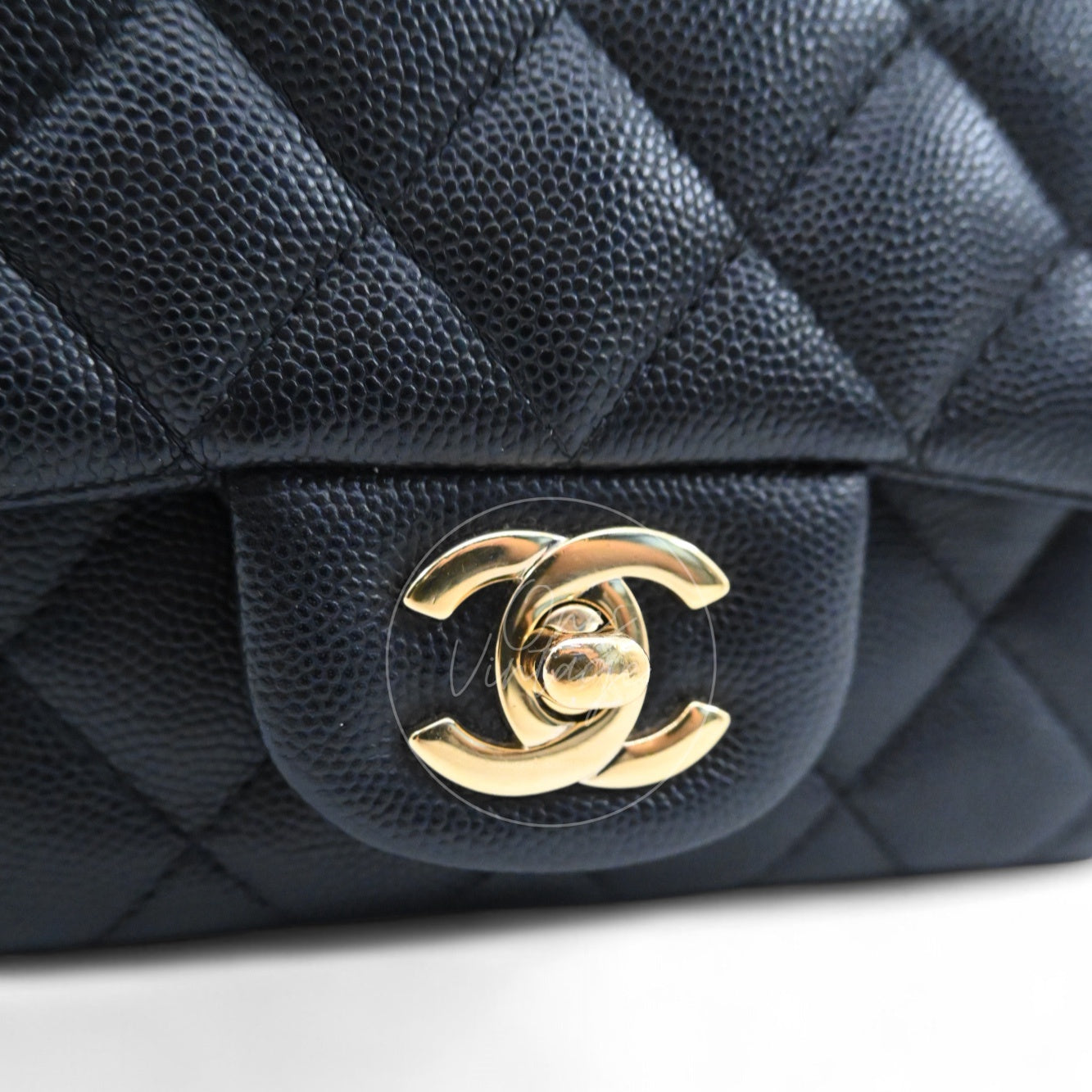 Close-up of modern light gold-tone interlocking CC turn-lock hardware on black caviar leather
