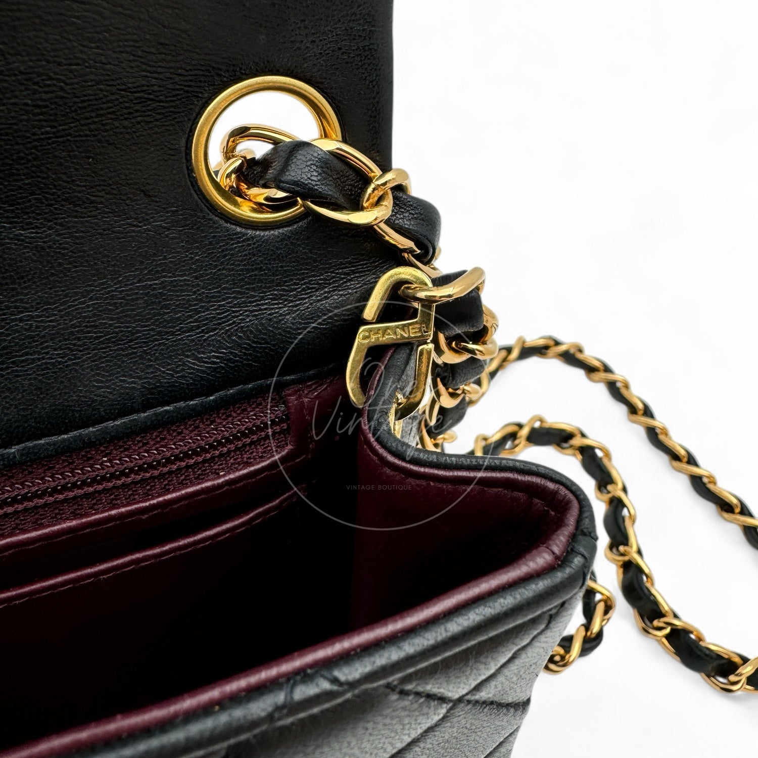 Close-up of gold-tone metal hook engraved with CHANEL and interwoven chain strap inside vintage bag