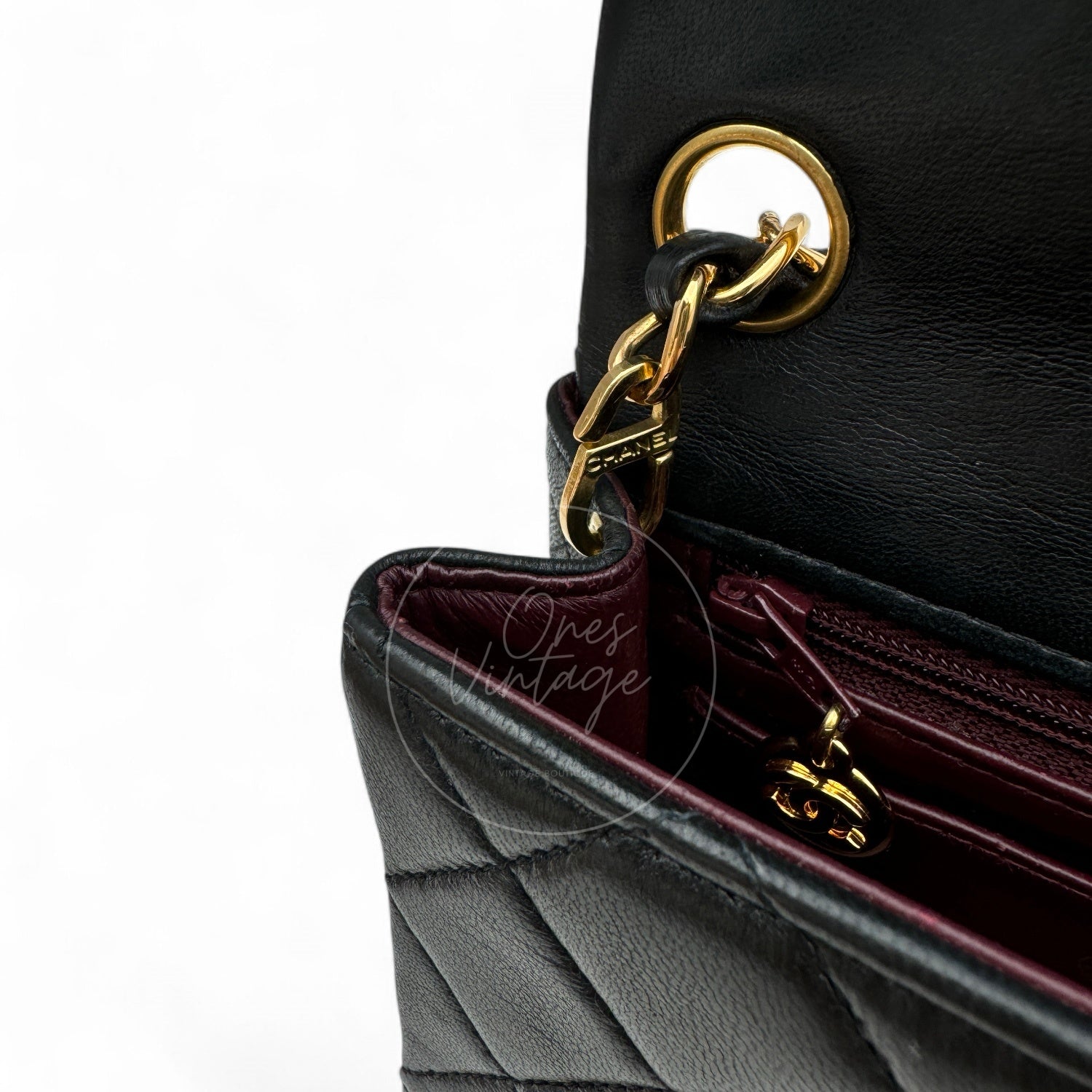 Close-up of small gold-tone CC logo zipper pull inside the burgundy leather lining of a vintage Chanel bag