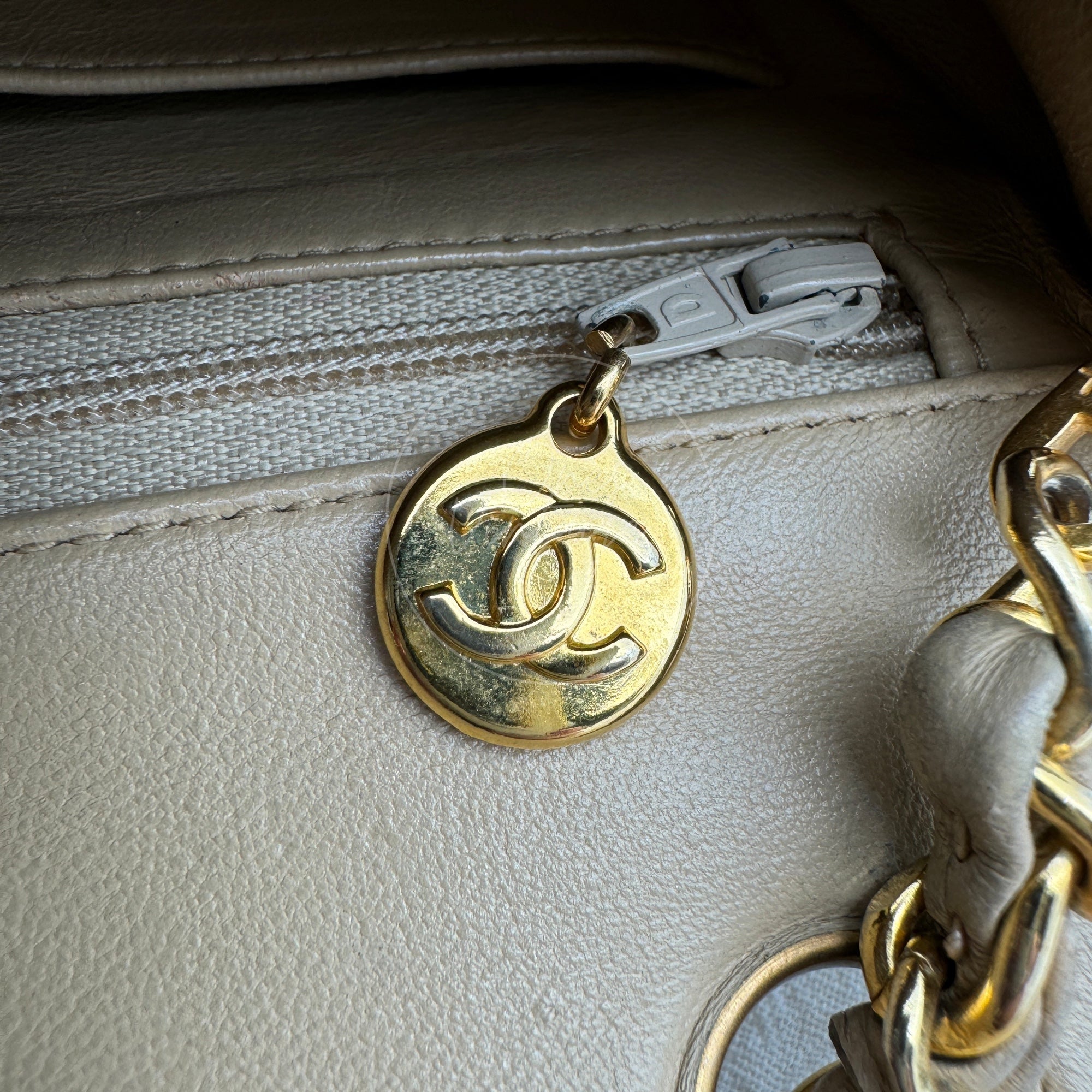Close-up of vintage gold-tone round zipper pull with CC logo inside beige Chanel bag